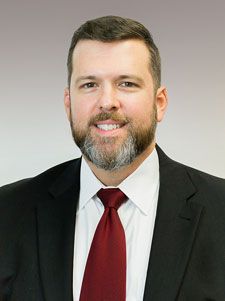 Headshot of Jake Brewbaker in a suit and tie